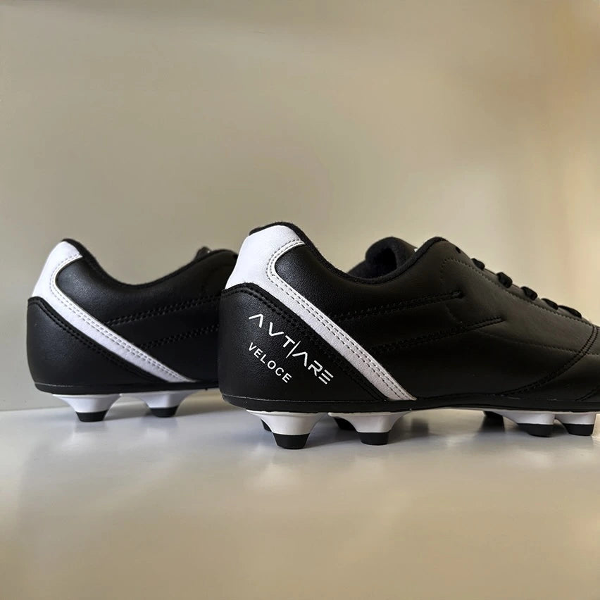 Pair of black and white soccer cleats with 'Avtiare' classico branding on a beige background