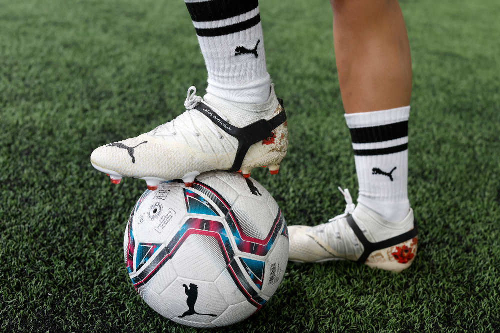 Person wearing Puma shoes and socks with a soccer ball on grass and wearing Playermaker Smart Sccer Tracker.